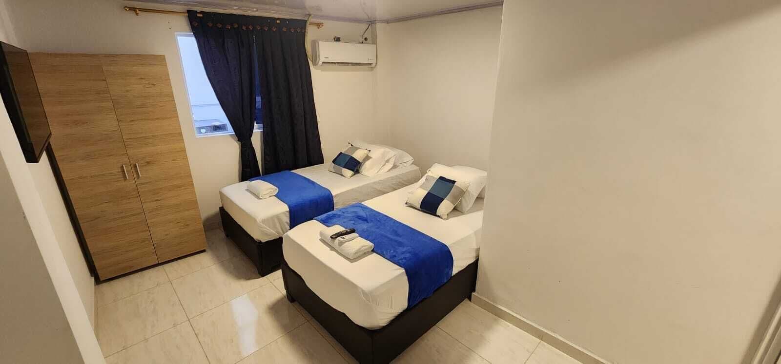 Una habitación pequeña y limpia con dos camas, un armario y una ventana con cortinas.