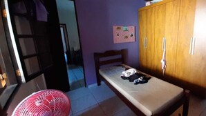 A room with a bed, a wooden wardrobe, a wall-mounted picture, and a red fan. - Casa Aconchegante em São Sebastião, Próxima ao Centro, Praias e Comércios (São Sebastião)