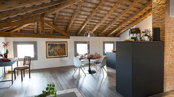 Un'ampia zona pranzo con soffitto in legno a volta e travi a vista, un tavolo rotondo con sedie e una parete in mattoni su un lato.