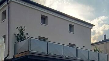 Un edificio a due piani con tetto piatto, un balcone con ringhiere in vetro e un ingresso a livello strada con facciata in legno.