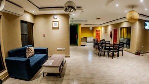 Eine moderne Hotelhalle mit einem blauen Sofa, einem Couchtisch, einer Essecke mit Holzstühlen und einer großen Hängeleuchte.