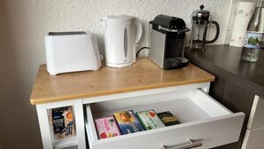 A kitchen counter with a coffee maker, a toaster, and a mug. There is a drawer below with some items. - Appartio-60m2-6 Pers-netflix (Hofheim in Unterfranken)