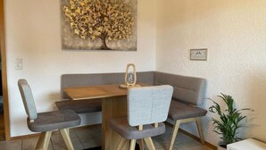 A dining area with a wooden table and four grey chairs. A painting of a tree is on the wall above the table. - Appartio-60m2-6 Pers-netflix (Hofheim in Unterfranken)
