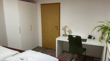 Une chambre d’hôtel avec un lit, un bureau et une chaise, une porte en bois et une plante en pot.