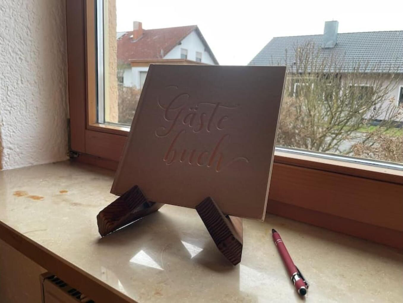 Ein Fensterbrett mit einem Ständer, der ein Schild mit der Aufschrift 'Gäste buch' und einen roten Stift daneben zeigt.