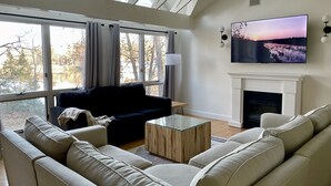 A modern living room with a large window, a fireplace, and a flat-screen TV mounted on the wall.