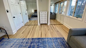 A room with a wooden floor, a blue patterned rug, a white dresser, and a gray sofa.