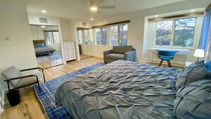 A bedroom with a large bed, a desk, a chair, a dresser, and a mirror.