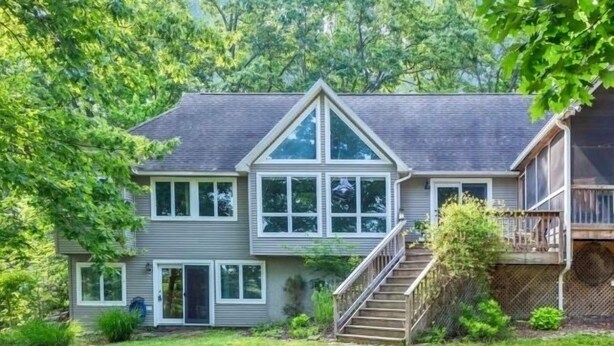 A two-story house with a front deck and a fire pit in the yard.