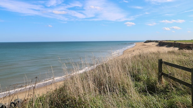 A beach with a wooden fence, grassy dunes, and a clear sky.