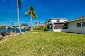 A modern house with a large lawn, a pool, and a view of the water. - 18116 Cutlass Cozy Pet Friendly Canalfront Home (Fort Myers Beach)