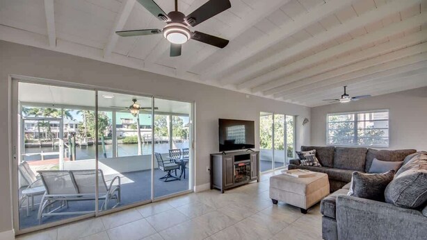 A spacious living area with a sliding glass door leading to an outdoor patio, a ceiling fan, a flat-screen TV, and a grey sofa. - 18116 Cutlass Cozy Pet Friendly Canalfront Home (Fort Myers Beach)