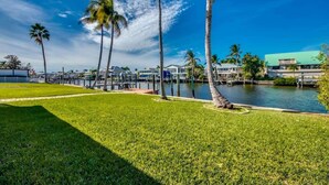 A waterfront property with a grassy lawn, palm trees, and a body of water. - 18116 Cutlass Cozy Pet Friendly Canalfront Home (Fort Myers Beach)