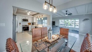 A modern living room with a glass coffee table, wicker furniture, and a kitchen in the background. - 18116 Cutlass Cozy Pet Friendly Canalfront Home (Fort Myers Beach)