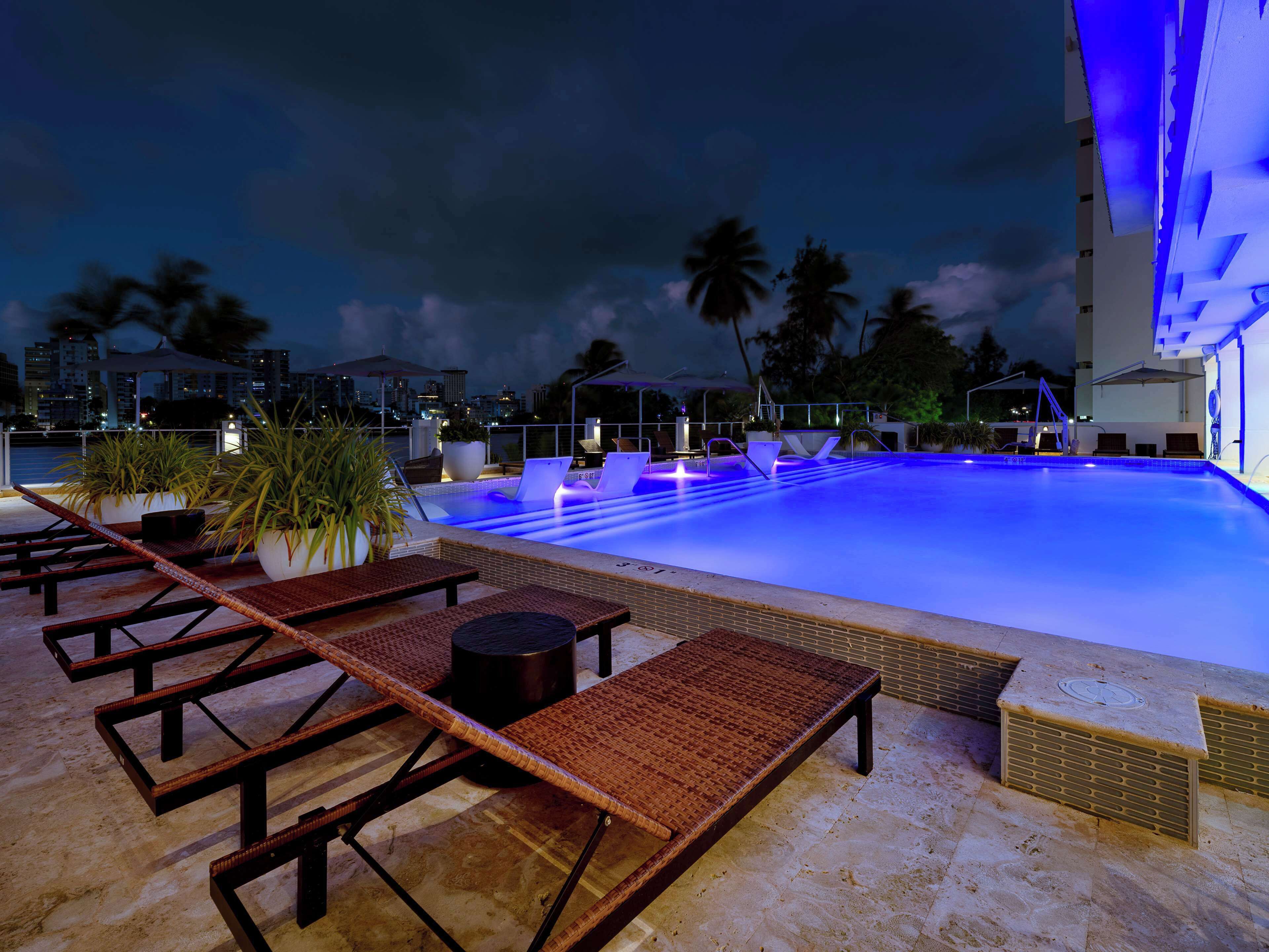 Una piscina al aire libre, sombrillas, sillones reclinables de piscina