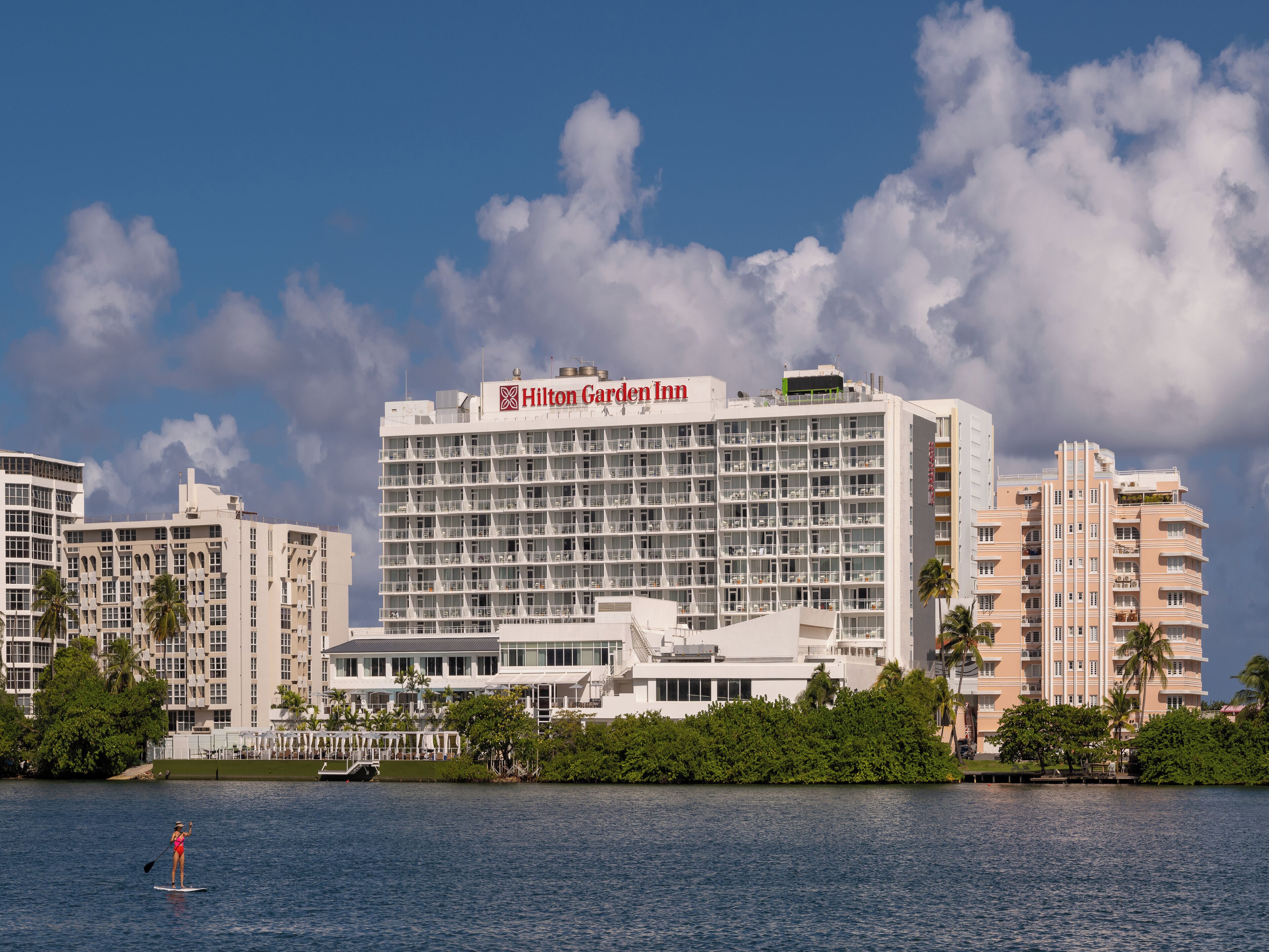 Ein Hilton Garden Inn Hotel mit moderner Architektur, in der Nähe eines Gewässers, im Vordergrund eine Person beim Paddleboarding.