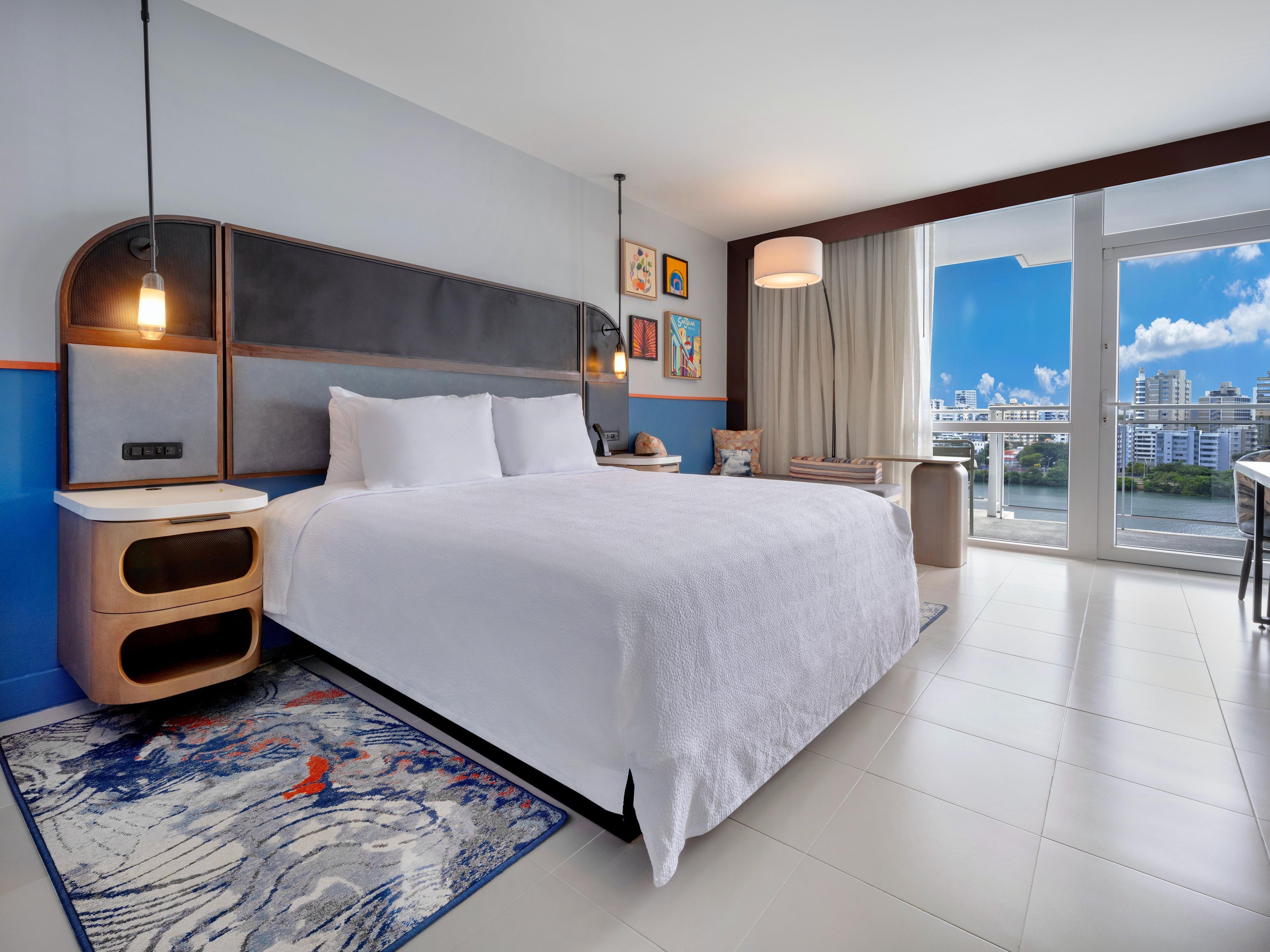 Une chambre d’hôtel moderne avec un grand lit, une table de chevet, un bureau et une vue sur la ville.