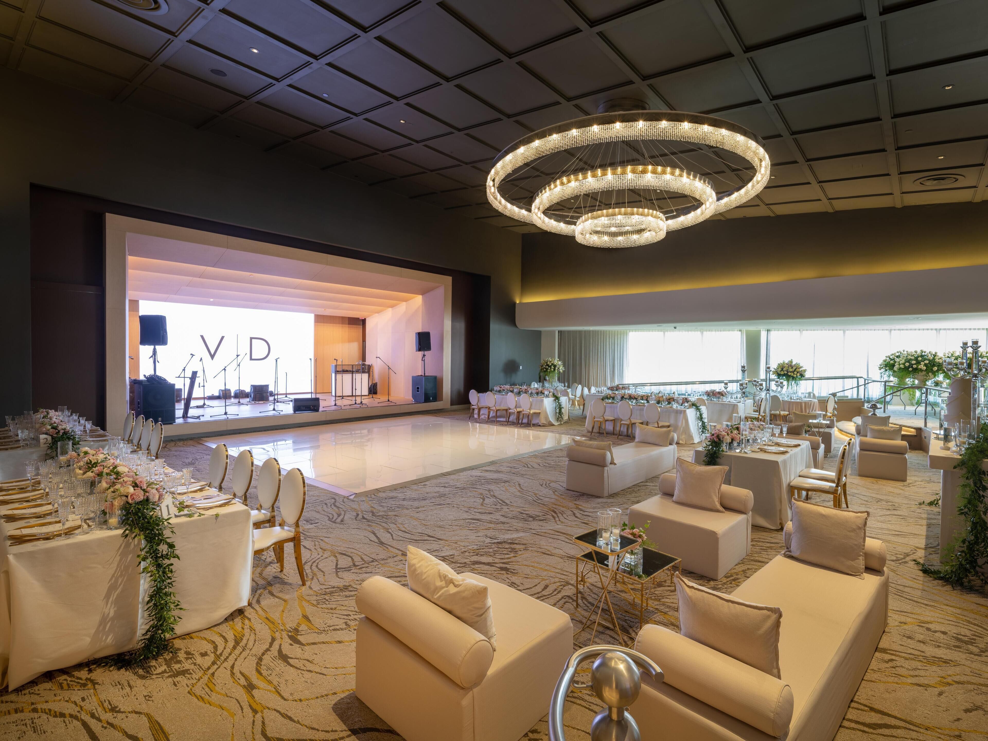 A spacious hall with a stage, seating arrangements, and a chandelier.