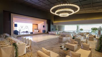 A spacious hall with a stage, seating arrangements, and a chandelier.
