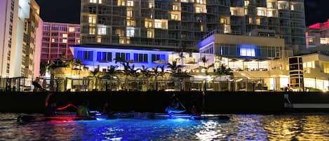 A waterfront hotel with multiple balconies and a pool area with illuminated water.