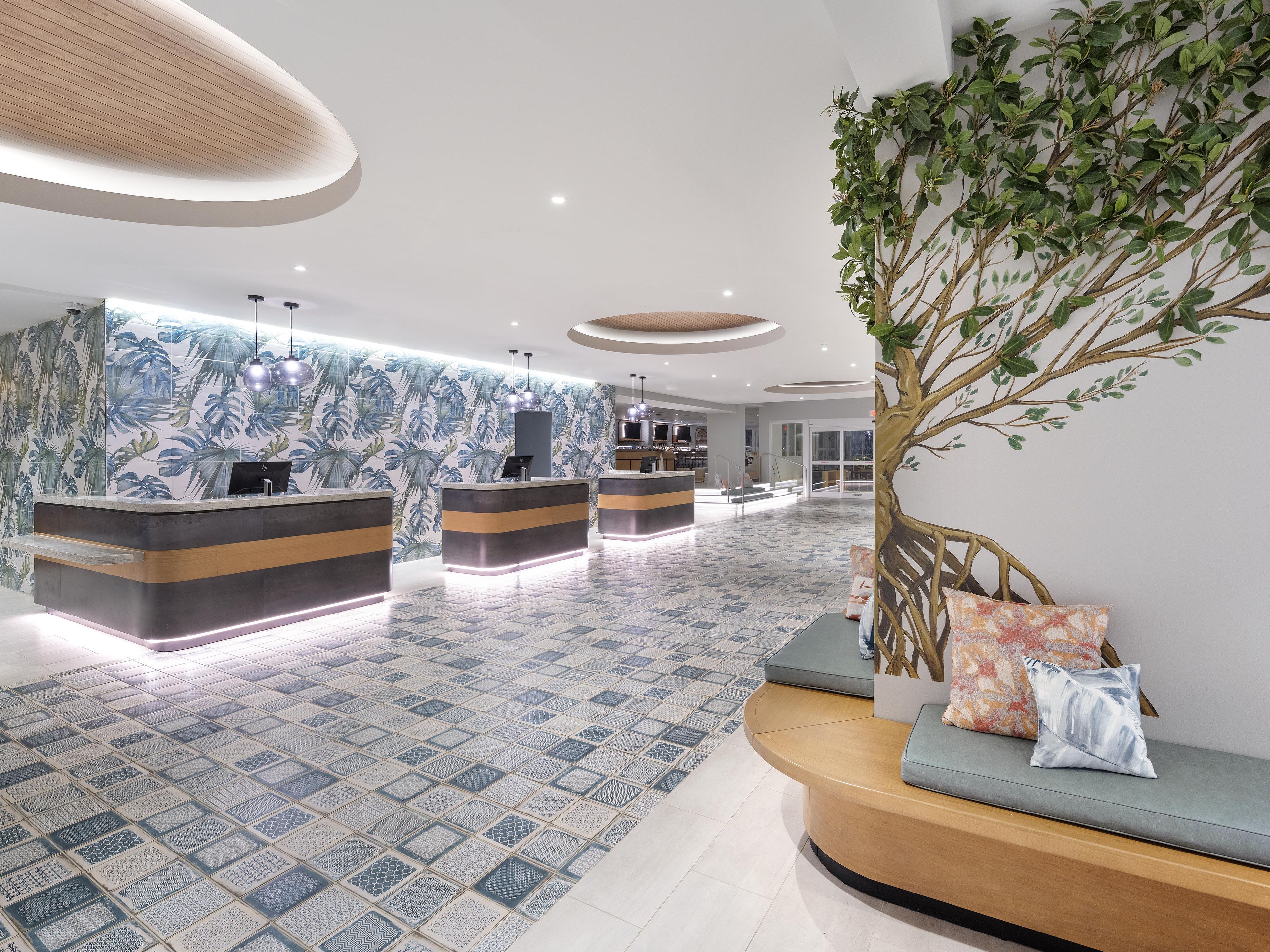 A hotel reception area with a modern design, featuring a reception desk, seating area, and a large plant.