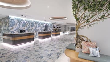 A hotel reception area with a modern design, featuring a reception desk, seating area, and a large plant.