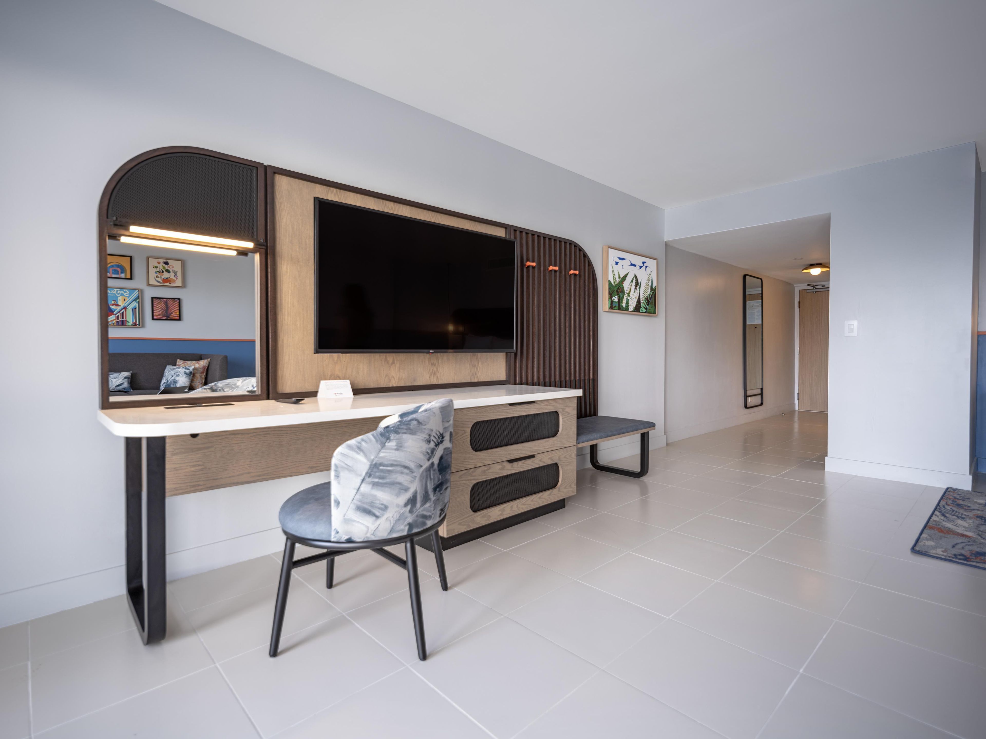 Un salón moderno con un televisor de pantalla plana grande montado en una pared de madera, una butaca tapizada de gris y una consola blanca con cajones.