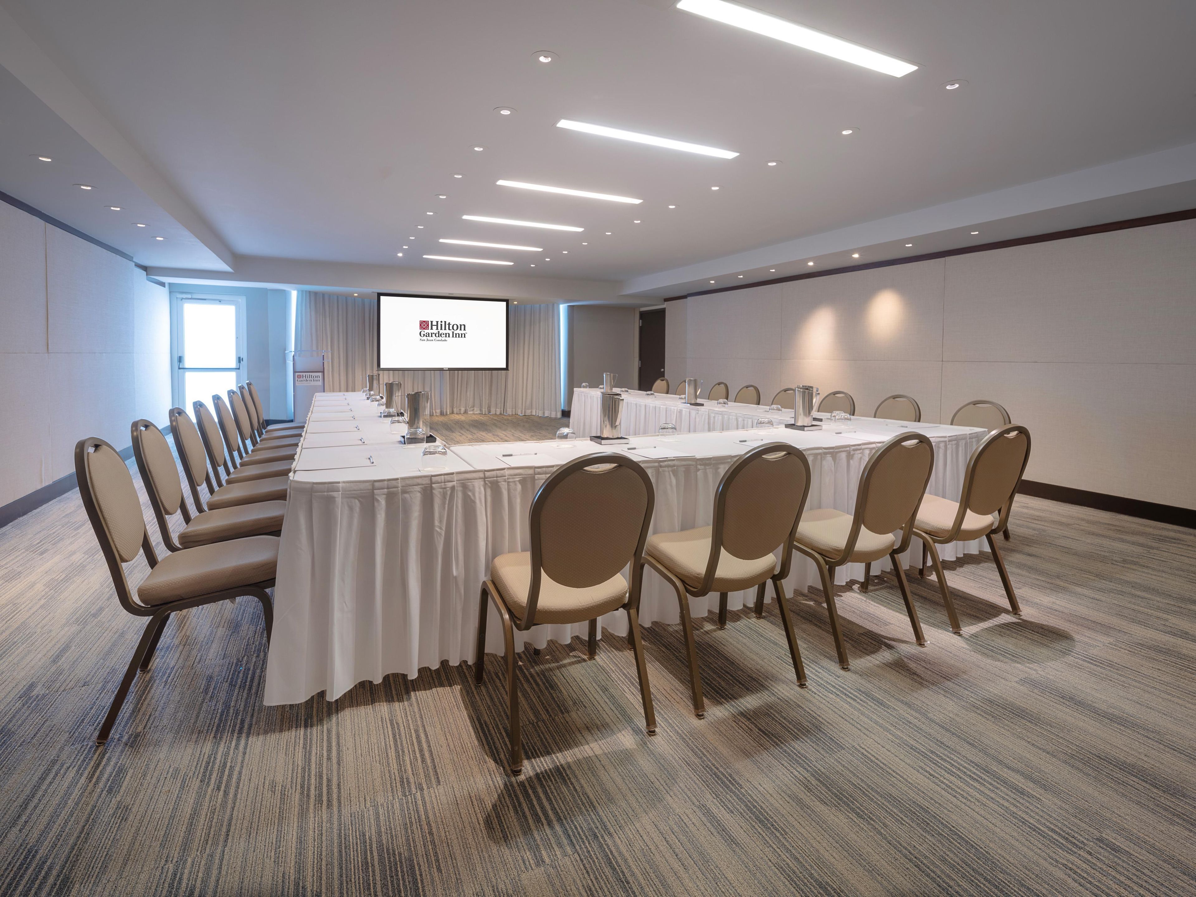 Une salle de conférence avec une longue table, des chaises, un écran de projection et un sol recouvert de moquette.