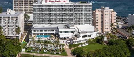 A large hotel with multiple floors, a swimming pool, and a view of the ocean.