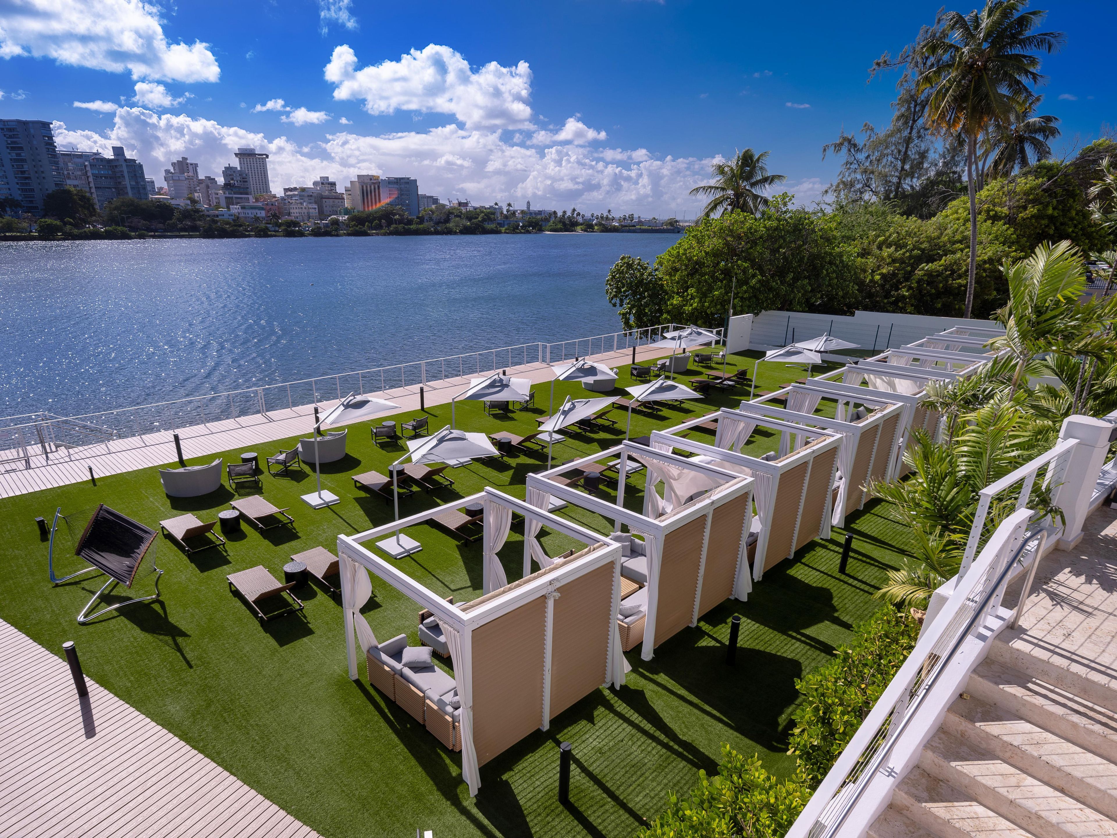 A rooftop terrace with sun loungers, a pool, and a view of the city skyline.