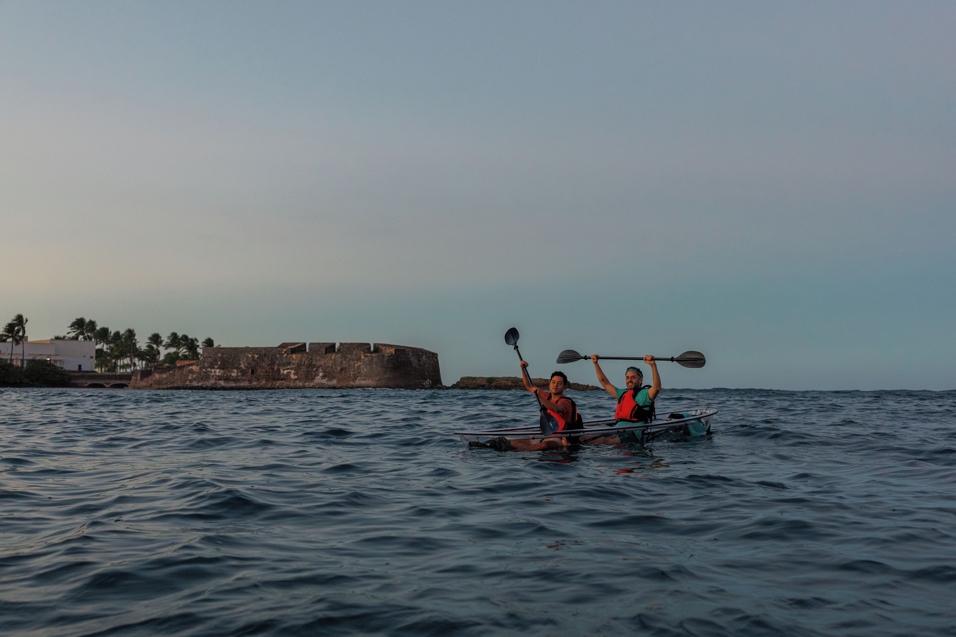 Deux personnes pratiquent le kayak sur une étendue d’eau calme, avec un fort historique en arrière-plan.