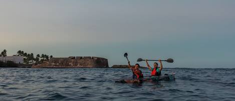 Dos personas remando en kayak sobre aguas tranquilas, con una fortaleza histórica al fondo.