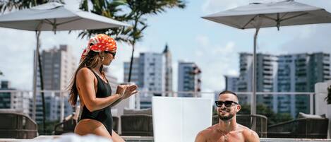 Un hombre y una mujer en una piscina, con sombrillas y palmeras al fondo.