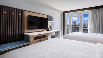 Habitación de hotel con una televisión de pantalla plana grande, un escritorio con una silla, un sofá y un balcón con vista a la ciudad.