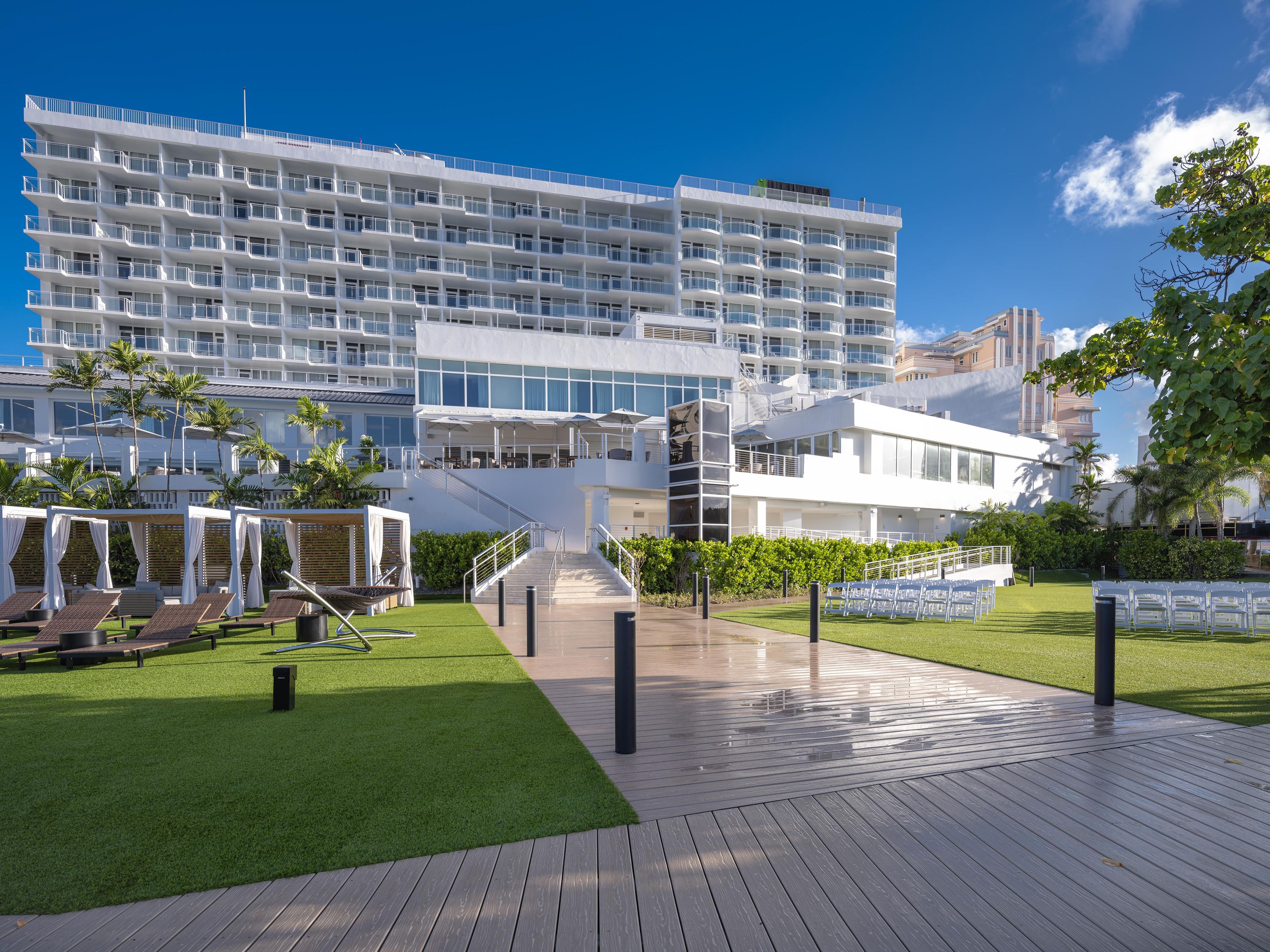Un hotel moderno con varios balcones, una zona de piscina con tumbonas y un jardín bien cuidado.
