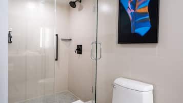 Une salle de bain moderne avec une douche à parois de verre, des toilettes blanches et une œuvre d’art encadrée au mur.