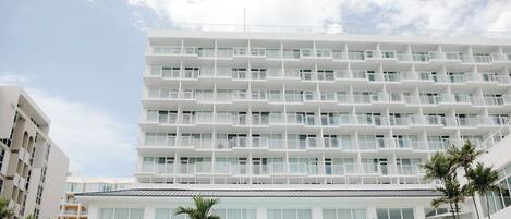 A multi-story hotel with balconies, large windows, and a pool area with umbrellas.