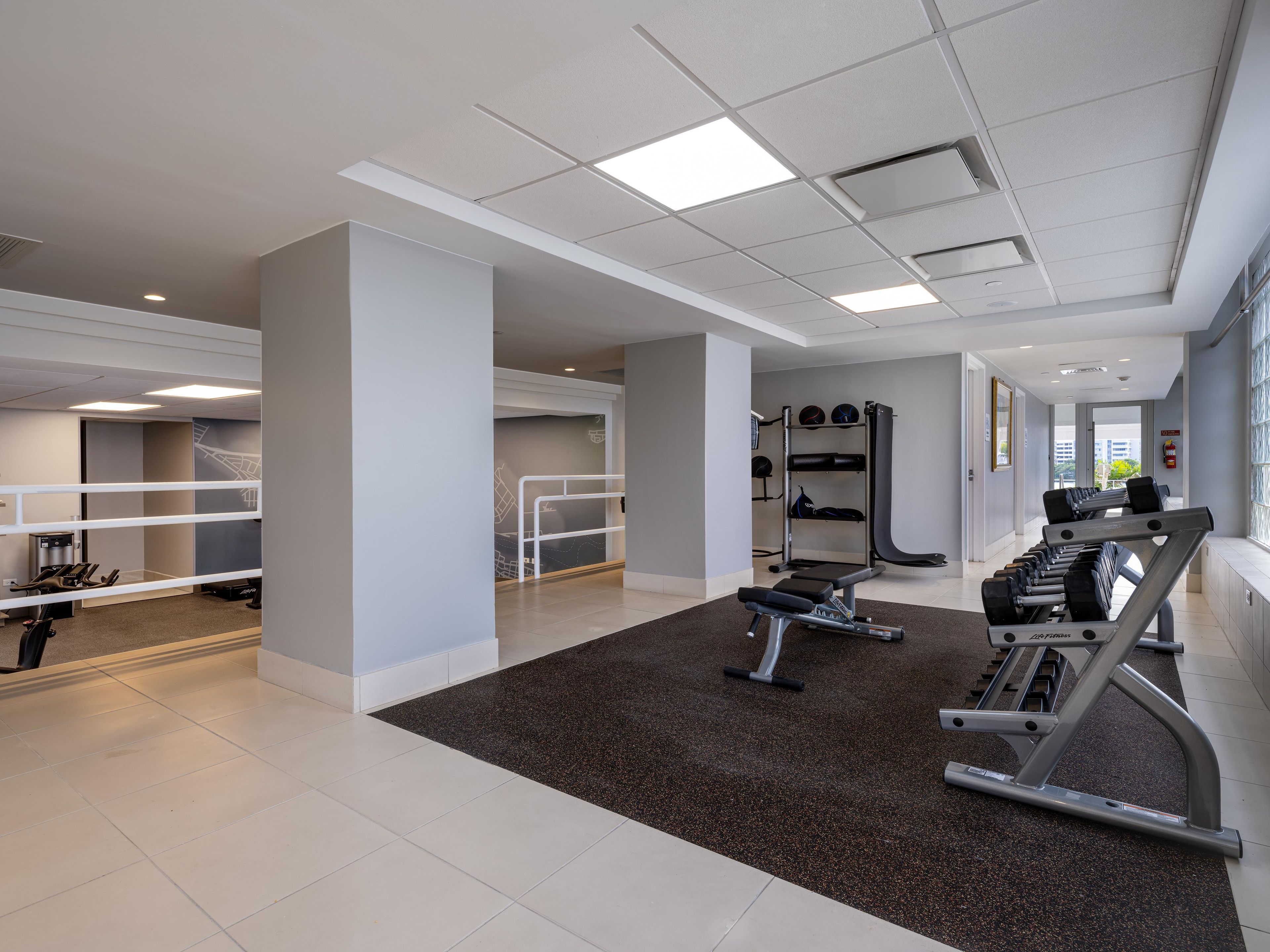 A gym with exercise equipment, a black rubber mat, and a white ceiling.