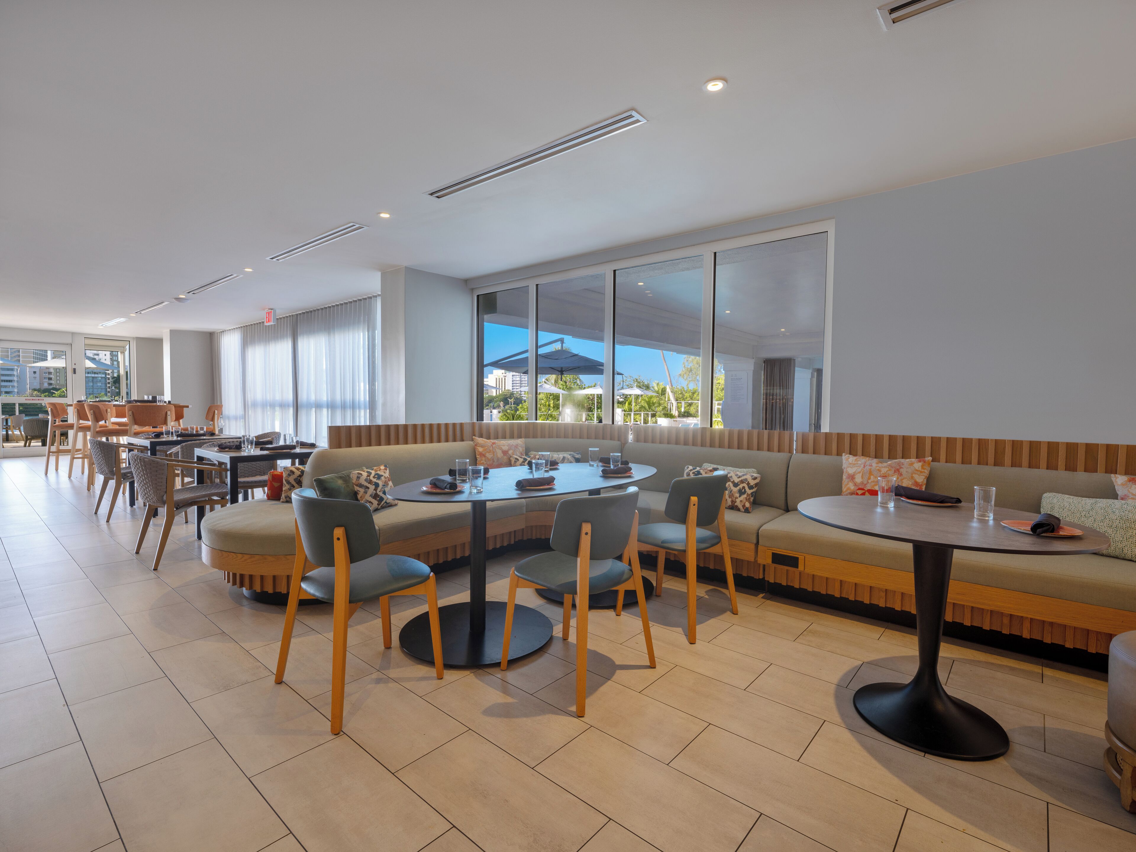 A modern dining area with round tables and cushioned seating, large windows offering views of the city, and a clean, contemporary design.