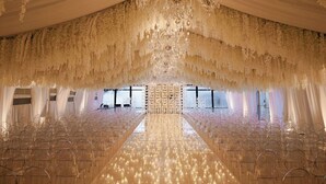 Un salón de banquetes con una larga mesa, sillas transparentes y una araña de cristal.