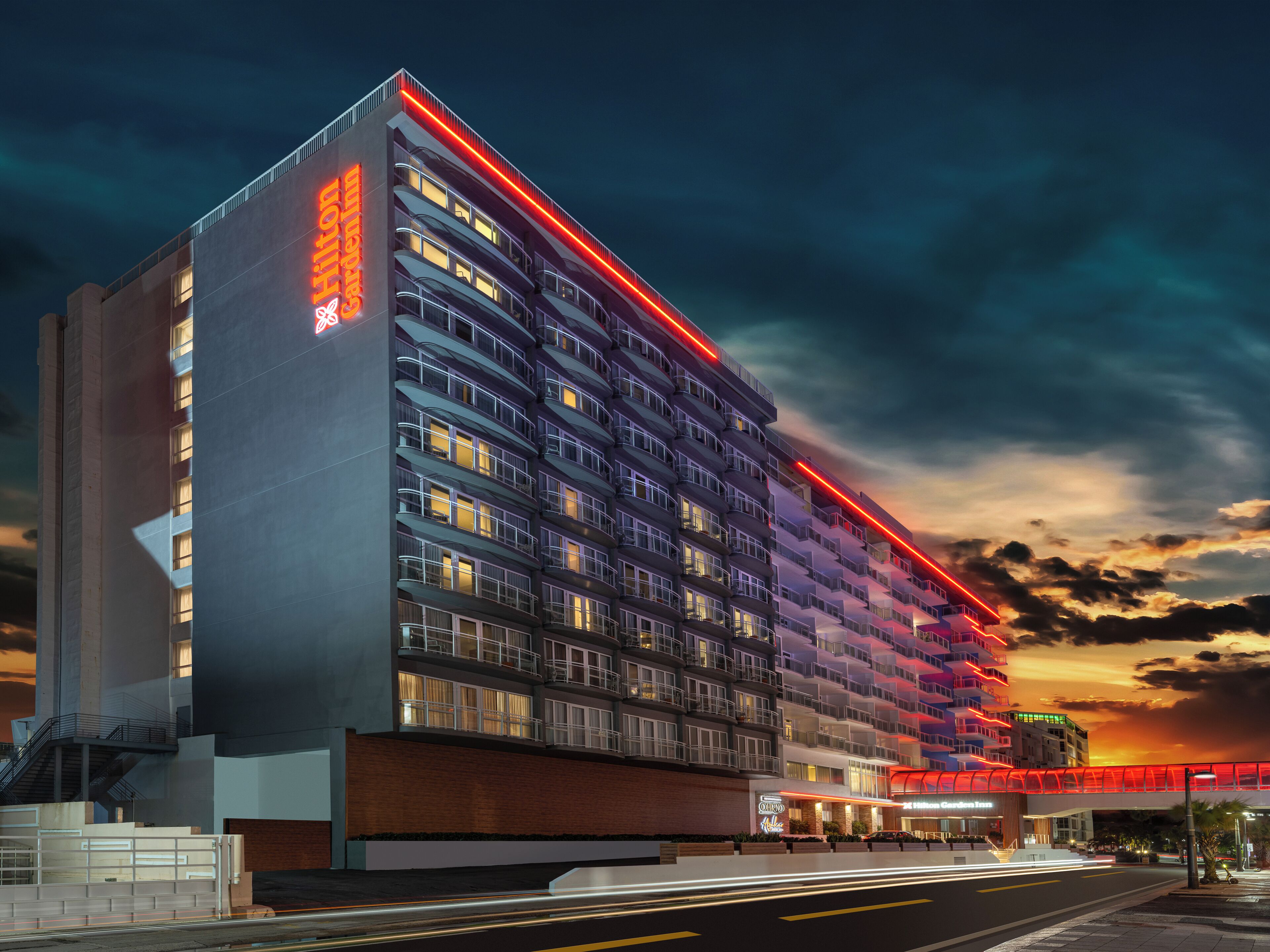 Un hôtel à plusieurs étages au design moderne, doté de balcons et d’une grande enseigne au néon rouge bien visible.