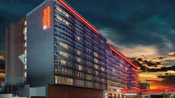 Un hôtel à plusieurs étages au design moderne, doté de balcons et d’une grande enseigne au néon rouge bien visible.