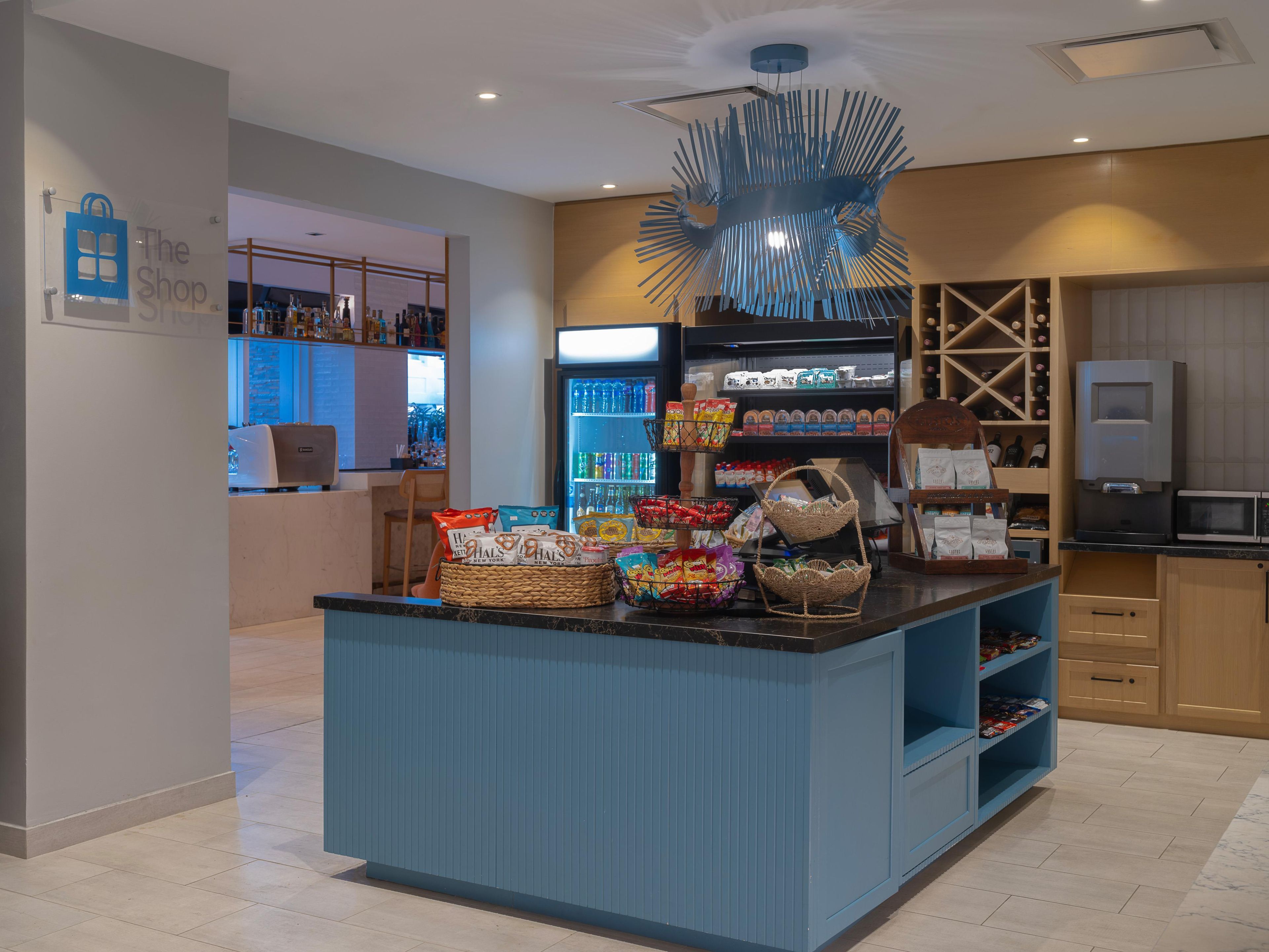 Un área de recepción con mostrador azul, cestas de aperitivos, un refrigerador lleno de bebidas y una exhibición de botellas de vino.
