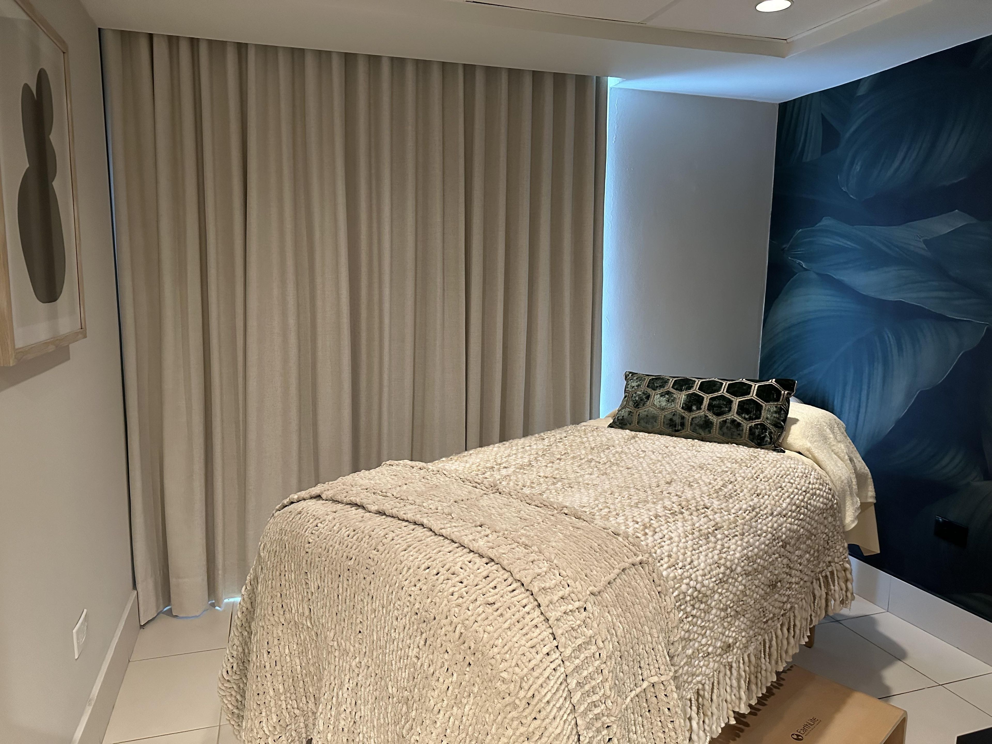 Un dormitorio con una cama, un ventanal con cortinas, una pared con diseño de hojas y un cuadro pequeño.