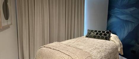 Un dormitorio con una cama, un ventanal con cortinas, una pared con diseño de hojas y un cuadro pequeño.