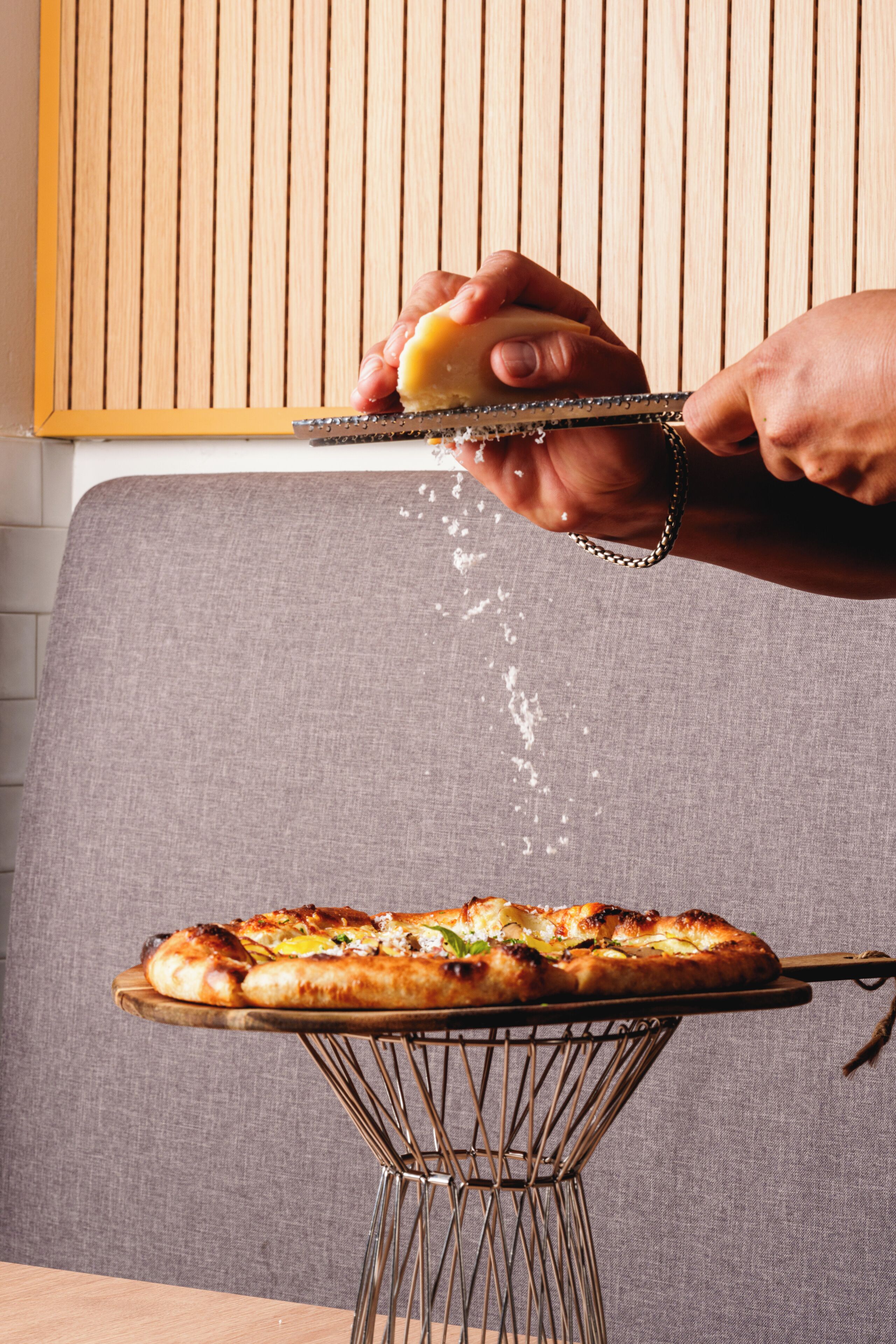 Una persona grattugia formaggio su una pizza su una griglia metallica.