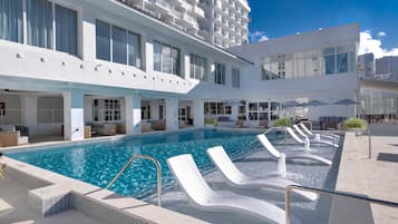 Un hotel moderno con zona de piscina, tumbonas y un área de estar cubierta.
