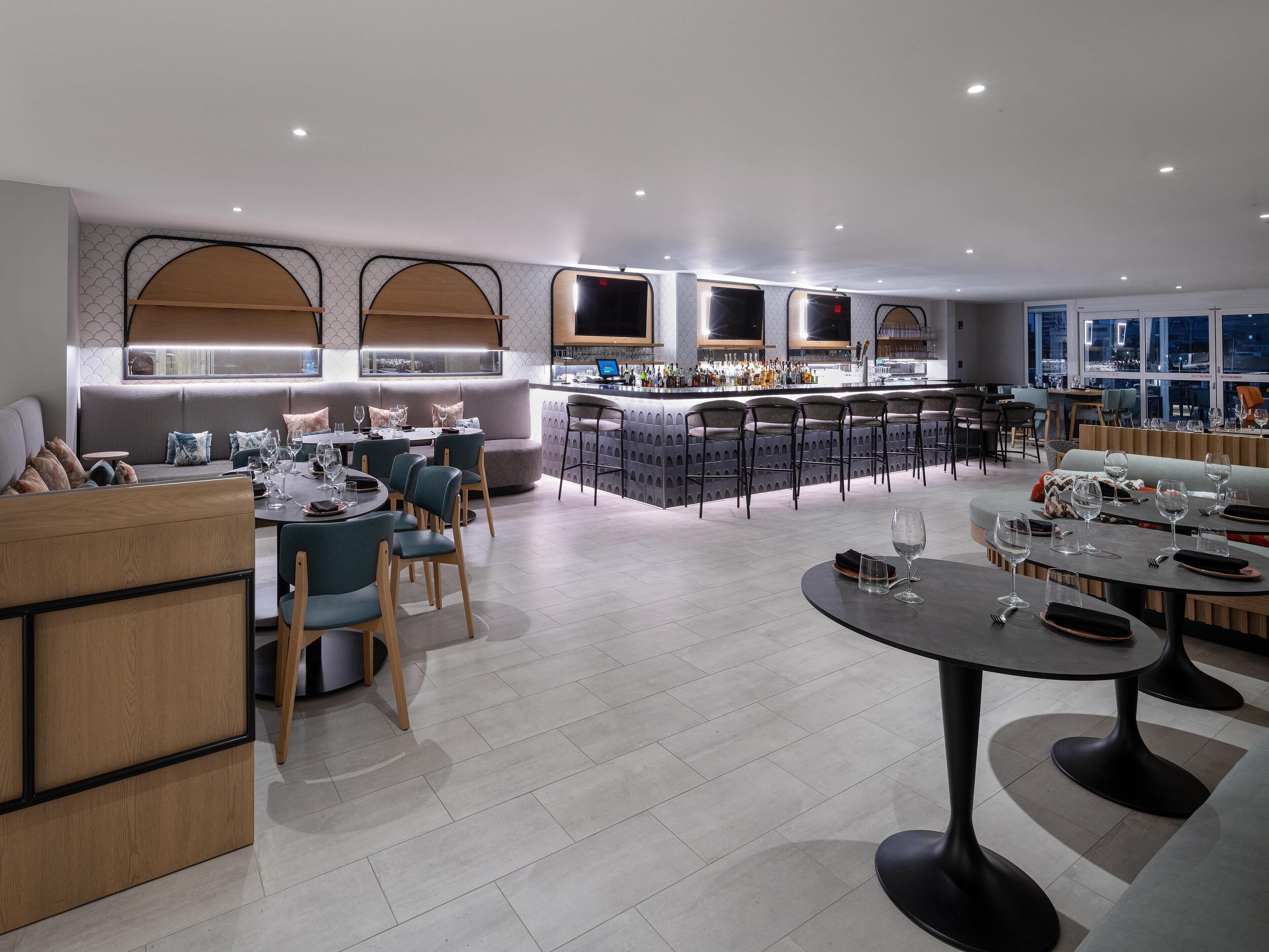 A modern interior with a bar area, seating arrangements, and a view through large windows.