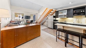 Una cocina moderna con una isla central, escalera de madera y electrodomésticos integrados.