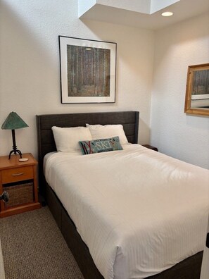 A neatly made bed with white bedding, a dark headboard, and a single pillow with a colorful design.